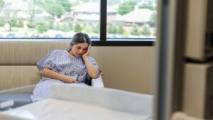 Young Woman Looks Sad While Sitting in the Corner While Wearing Hospital Gown