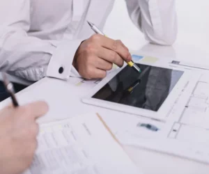 People discussing inside an office. One using the tablet and the other using paper with pen.