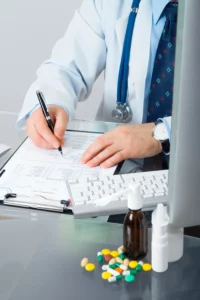 Doctor writing on his desk on a paper with pills and a computer monitor on them